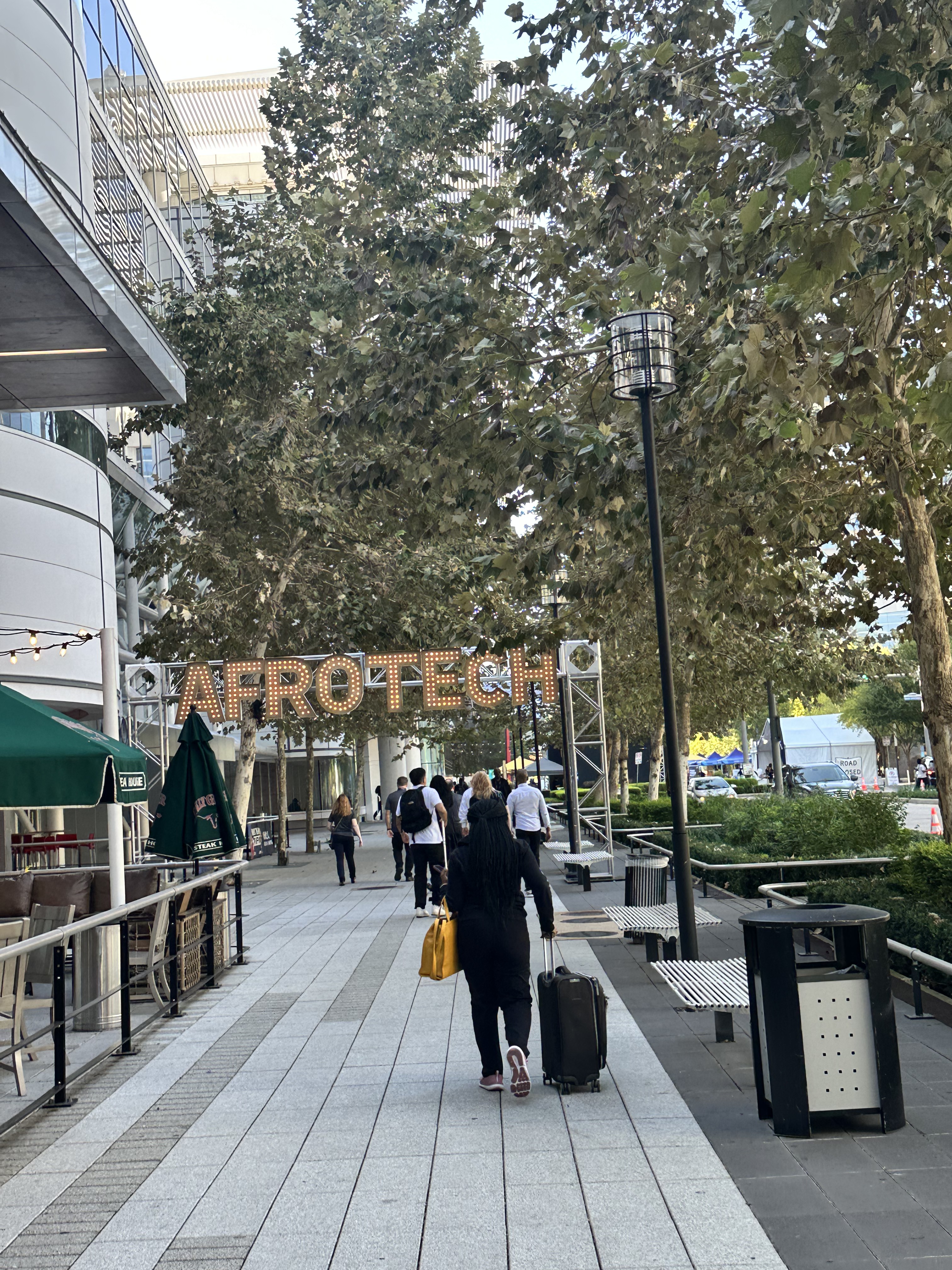 An illuminated AfroTech entrance beneath trees and city buildings at dusk.